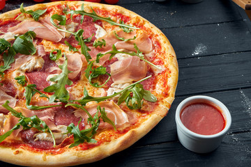 Baked pizza with salami, prosciutto and chicken with red sauce and melted cheese on a black wooden...