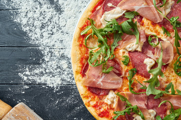 Baked pizza with salami, prosciutto and chicken with red sauce and melted cheese on a black wooden...