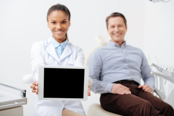 selective focus of smiling african american dentist holding digital tablet with blank screen near happy patient