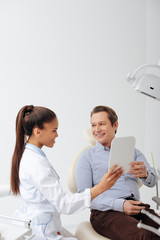 Fototapeta premium happy patient looking at mirror near smiling african american dentist in braces