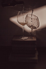 Fototapeta na wymiar white wine is poured into a glass that stands on a stack of books 