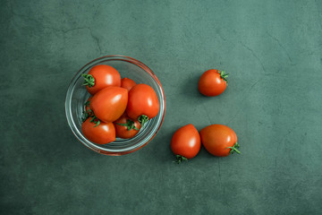 Cherry tomatoes in glass bowl on stone, concrete background. Freshly harvested delicious, healthy and organic vegetables. Flat lay, top view.