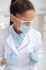 african american dentist in medical mask, face shield and latex gloves