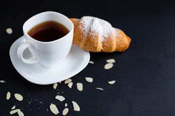 Coffee white cup, croissants on dark background. Breakfast concept..White cup with coffee and croissant stands on a black background. A cup of hot black coffee.