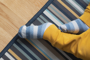 Baby feet with striped socks laying on wooden floor with rug