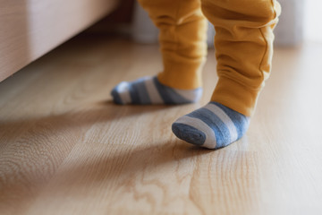 Baby feet with striped socks, standing and trying his first steps, selective focus