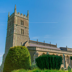 A close up of an English church in the Somerset countryside in the South West of England on a bright sunny day.  The background is a bright blue sky and a plane flies across behind the church.