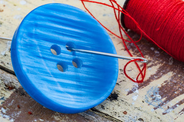 Close up on blue button with needle and red thread