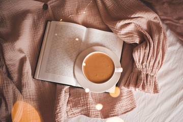 Cup of tasty coffee on open book in bed closeup. Top view. Good morning.