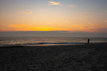 ein Mann mit seinem Hund ist am Abend alleine am Strand unterwegs