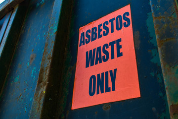 Asbestos Waste Only warning sign on a dark rusty old construction container.