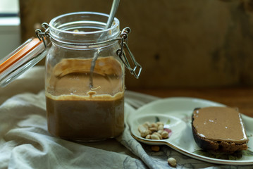 Glass jar with peanut butter. Slice of bread with peanut butter and coffee. Still life. Morning.
