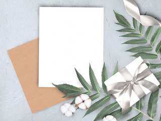 Mock up concept  with empty blank, envelope, gift, cotton flowers and leaves on grey background. Elegant still life flatlay for Mothers day, Womans day or wedding invitation.