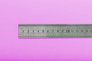 A metal ruler with a scale on a pink background is a superscape with a copy of the space for your...