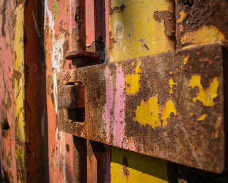 A rusty old mechanism to open a shipping or construction unit.  The container is covered in rust and painted in pink, yellow and red.