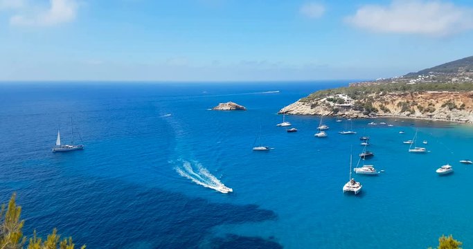 famous, beautiful beach at daylight with calm sea, in summer very popular, sandy coast have a fantastic view of island of ibiza. Moored vessels on bay. Ibiza Island, Balearic Islands