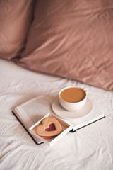 Cup of coffee with heart shape cake in bed closeup. Good morning. Breakfast.