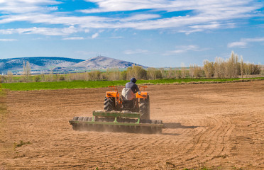 Back view of a tractor working in the field and blue sky in background.