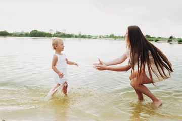 Fototapeta premium beautiful mother with baby daughter are having fun and playing near the lake. The concept of summer holiday. Mother's, baby's day. Spending time together. Family look. Sun light. selective focus