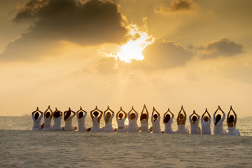 Obraz premium Yoga silhouette of a young people doing yoga during colorful sunset at the beach by the ocean coast. Concept of healthy life and natural balance between body and mental development.