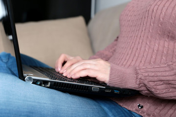 Woman in jeans sitting on a sofa with a laptop on her lap. Concept of freelancer, remote work from home, online business during coronavirus quarantine