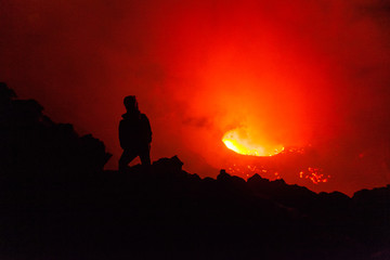 Fototapeta na wymiar A person standing in front of the lava lake at night