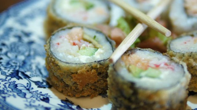 Sushi Macro rolls Chopsticks in Plate. Uramaki Japanese dish made of Rice Salmon Vasabi Tuna in soy. Oriental tradition. Close-up Isolated.