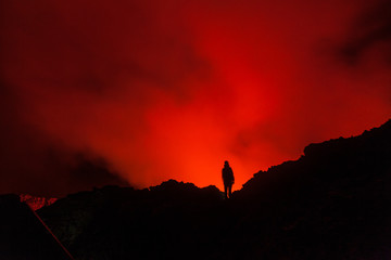 Glowing lava inside the crater of Nyiragongo volcano lights up the sky around a tourist