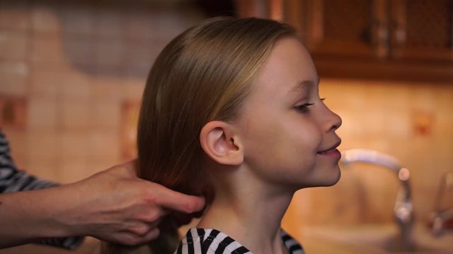 Caring mother stroke daughter child long hair with hands start to make braid with weave hairstyle wearing striped dress at wooden kitchen cosy home. Mom cares. Mother Day
