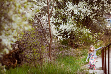 Naklejka na ściany i meble small girl climbs up stairs along flowering trees