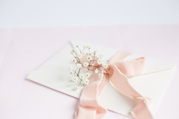 Envelope on a white-pink background with peach silk ribbon and pink flowers. Wedding invitation. Mother's day card. Place for text. Copy space