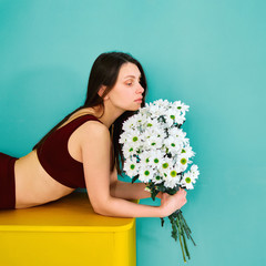 A young girl in sportswear is lying on a yellow chest of drawers with flowers in her hands