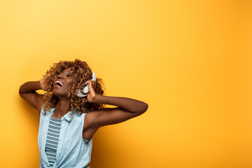 happy african american woman listening music in headphones on yellow background