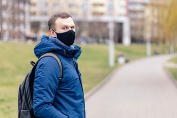 A young man in a black protective mask during the pandemic on a city street 