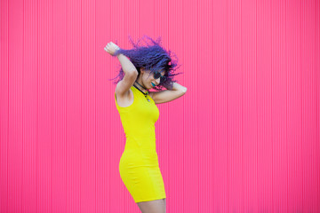 Young woman with urban lifestyle. Afro music rhythm and blues concept. Millennial woman dancing to pop music in the street isolated on pink background. Teenagers associated with fun bright colors.