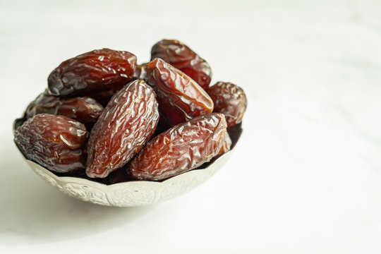 Raw date fruit ready to eat in silver bowl on a white marble background. Traditional, delicious and healthy ramadan food.