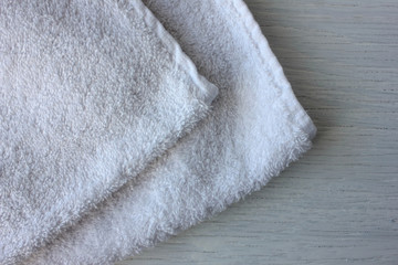 Fototapeta na wymiar Folded soft cotton white towel on a white wooden table. Terry fabric bath towel texture.