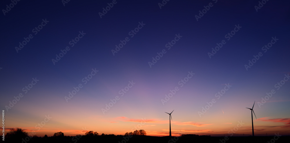 Wall mural late evening sunset with dark blue sky and 2 windmills to produce electricity