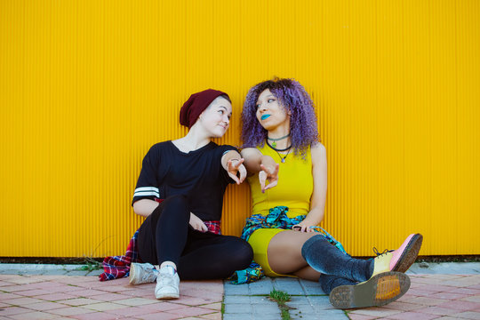 Teen girlfriend couple bonding together outdoors. Millennial gay woman with ethnic girlfriend isolated on a yellow background. Lesbian and lgbt lifestyle concept for young people.
