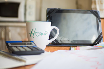 On the home table are stock and finance charts with a calculator, a coffee mug, a pencil, a marker pen, two notebooks, a smartphone and a tablet for remote work. Work at home.