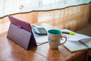 On the home table are stock and finance charts with a calculator, a coffee mug, a pencil, a marker pen, two notebooks, a smartphone and a tablet for remote work. Work at home.