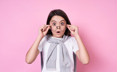 Cute fashionable emotional girl with glasses in a basic T-shirt on a pink background.