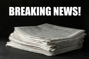 Phrase Breaking News and stack of newspapers on dark stone table. Journalist's work