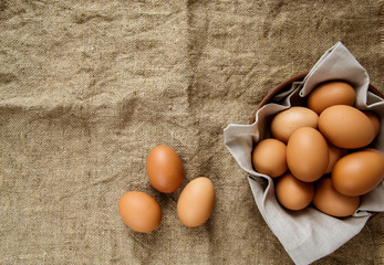 Chicken eggs in a clay plate with a linen napkin and three eggs on burlap. View from above. Copy space.