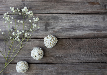 Obraz na płótnie Canvas Homemade raw chocolate truffles with nuts and chia seeds in coconut flakes on a wooden background, branch of white wildflowers, horizontal orientation