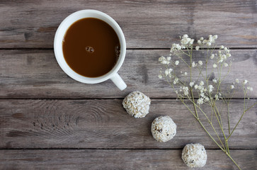 Obraz na płótnie Canvas Energy balls on a dark wooden background with a branch of white flowers and a cup of coffee, flat lay, copy space, concept of a healthy quarantine snack