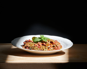 Beans and rye with mint leaves on a white plate, on a wooden chopping board, illuminated by direct sunlight