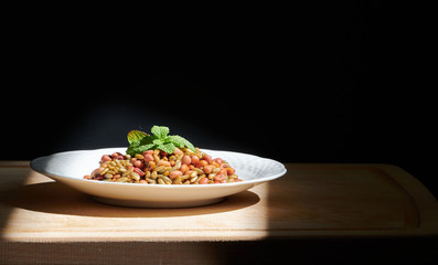 Beans and rye with mint leaves on a white plate, on a wooden chopping board, illuminated by direct sunlight