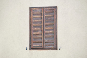 Italian window on the beige wall facade with closed brown color rolling shutters and pattern on both sides