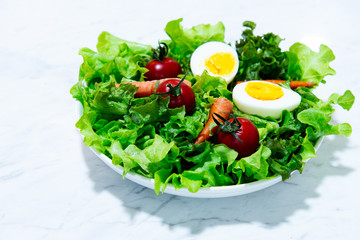 Tasty fresh mix vegetable salad on white dish and wooden plate.